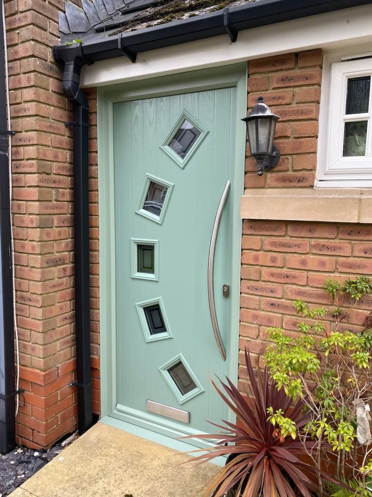 Light green composite front door with a curved glass style window and silver curved door handle.