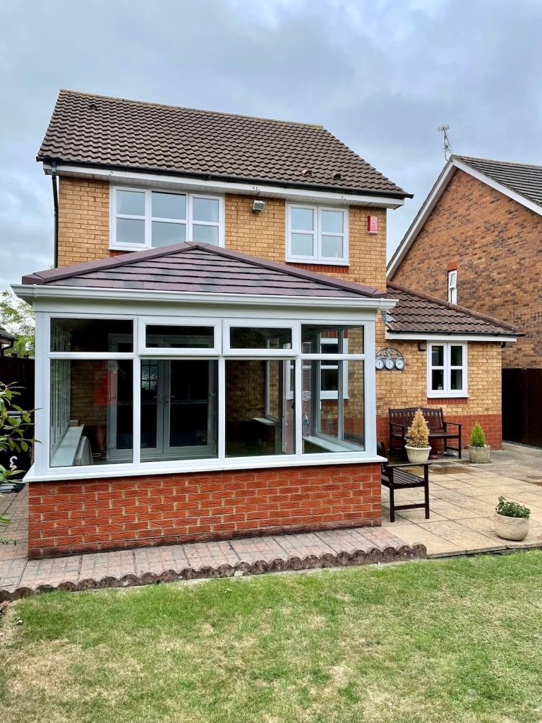 Modern tiled roof conservatory with white uPVC frames on a detached brick house.