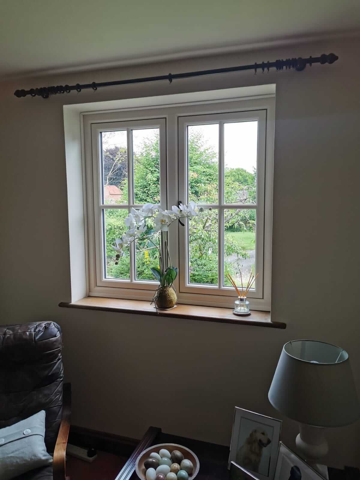 A flush sash window in a living room, framed by a cosy interior with a decorative window sill featuring a flower pot and reed diffuser. This image illustrates how energy-efficient flush sash windows enhance natural light and complement modern interiors.