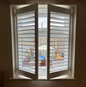 Partly open white shutters looking out on to the back garden.