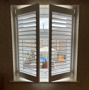 Partly open white shutters looking out on to the back garden.