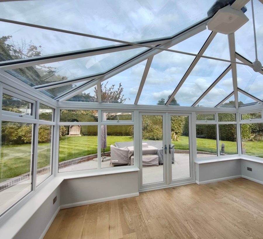 A bright conservatory interior with a glass roof and white uPVC frames, showcasing natural light and a connection to the surrounding garden. The image highlights the spacious and versatile design of a modern conservatory.
