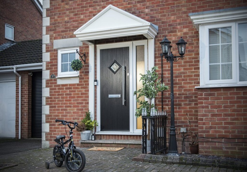 A modern black composite front door with side panel and large handle on a brick house.