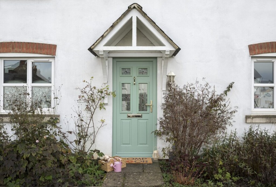 A pastel green composite front door with multiple glass panels on a white rendered house.
