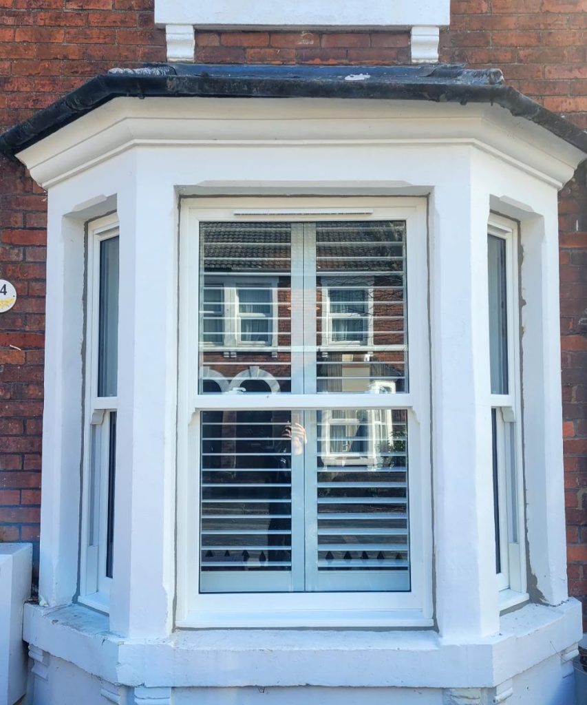 White uPVC bay window with sash design and shutters on a red brick house.