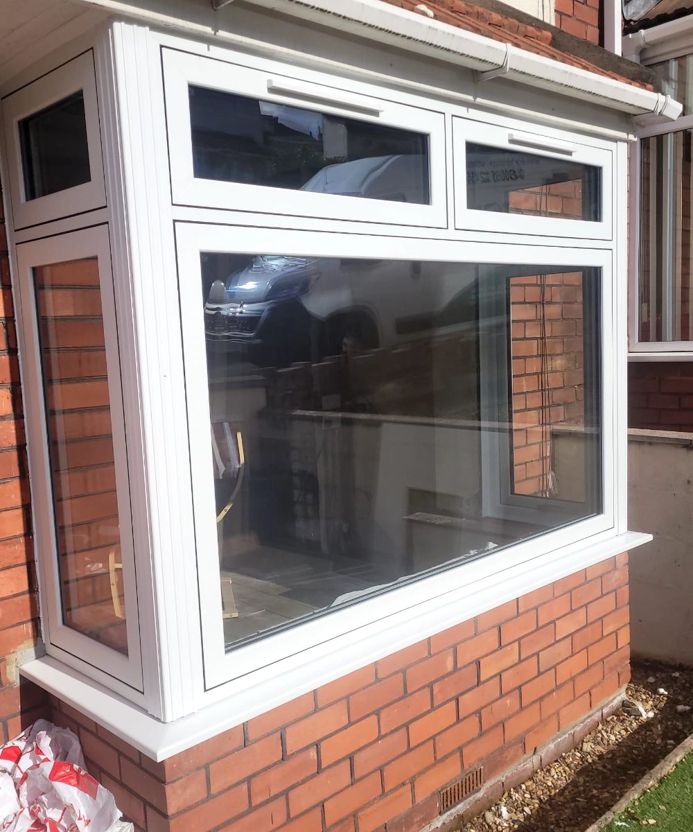 Modern white uPVC bay window with large glass panels on a red brick house exterior