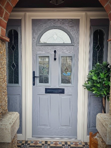 A detailed image of a new gray front door with decorative glass panels and a black handle/mail slot.